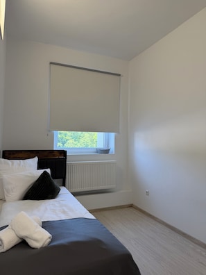 A bedroom with a bed, a window with a blind, a radiator, and a view of greenery outside.