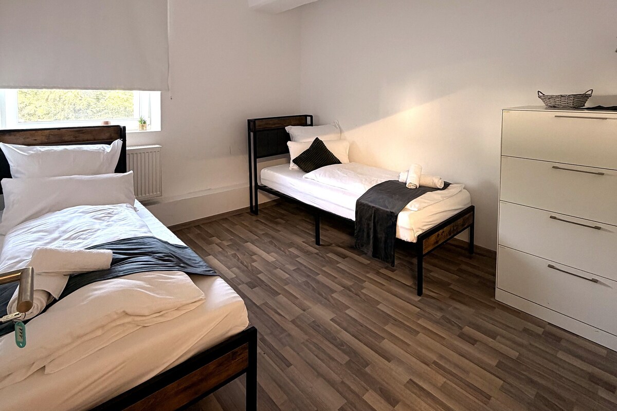 A bedroom with a large bed, a smaller bed, a dresser, and a window.