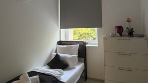 A small, single-bed room with a window, a bedside table, and a dresser.