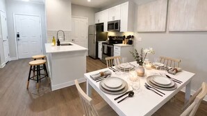 A modern kitchen with white cabinetry, a central island, and a dining area set for a meal. - Resort-Style 1BR, 4 Pools & Fitness, Free Parking (Scottsdale)