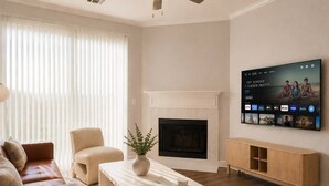 A modern living room with a fireplace, a flat-screen TV mounted on the wall, a sofa, a coffee table, and a sideboard. - Resort-Style 1BR, 4 Pools & Fitness, Free Parking (Scottsdale)