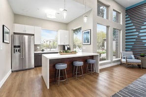 A modern kitchen with a central island, bar stools, and a large window providing a view of the outdoors. - N. Scottsdale Retreat | Hot Tub, Pools, W/D, Gym (Scottsdale)