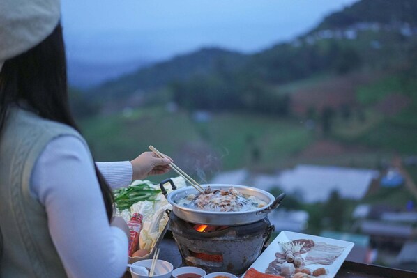 A person cooking outdoors with a portable stove, surrounded by food items and condiments.