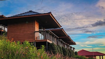 A wooden house with a balcony and a red-roofed structure in the background.