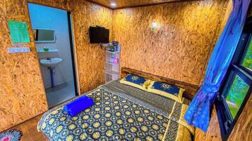 A room with a bed, a television, a sink, and a window with curtains.