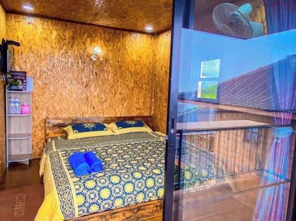 A room with a bed, a wooden wall, a shelf with items, and a window.