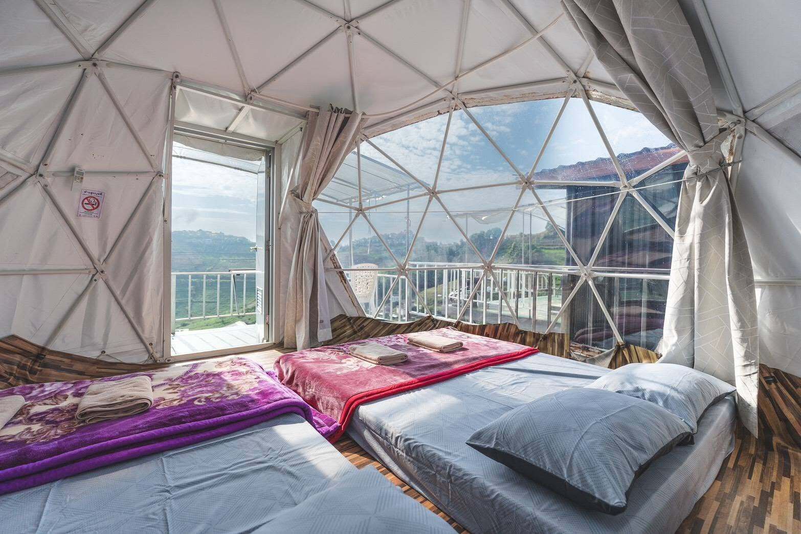 Alojamiento con tienda de campaña, dos camas, una ventana y vistas del paisaje.