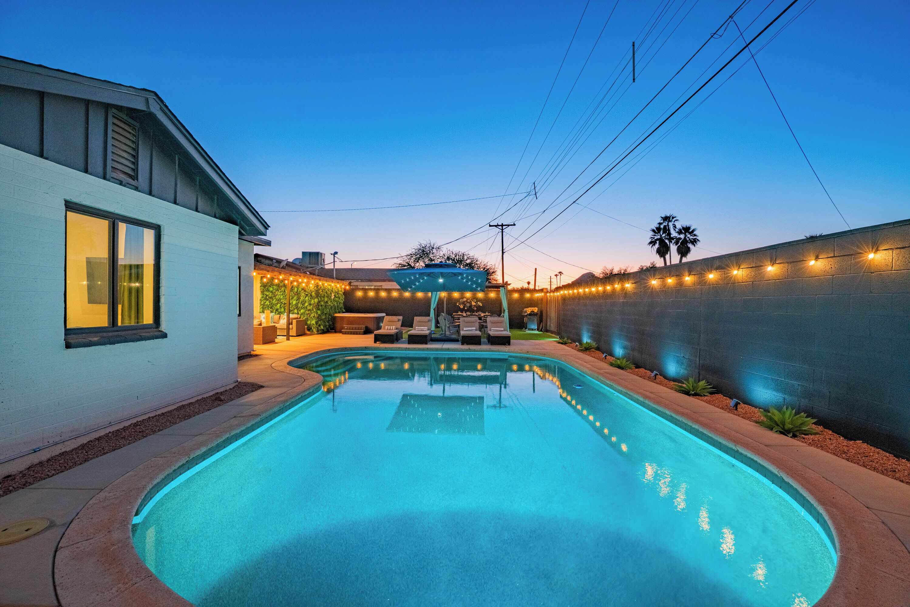 A swimming pool with a curved edge, surrounded by a patio area with outdoor furniture and string lights.