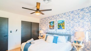 Un dormitorio con cama, dos mesitas de noche, ventilador de techo y una puerta.