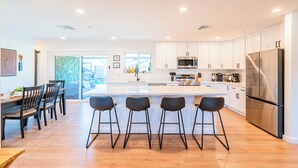 Una cocina moderna con armarios blancos, electrodomésticos de acero inoxidable y una isla central con taburetes de bar.