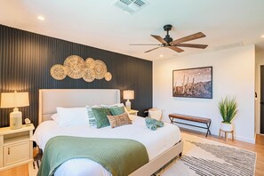 Un dormitorio moderno con una cama, mesitas de noche, un ventilador de techo, una obra de arte en la pared y un banco.