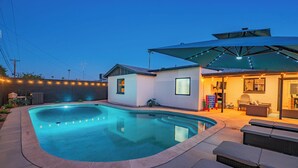 Una piscina de borde curvo, un área de patio con mobiliario exterior y un edificio con techo inclinado.