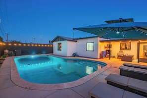 Ein Pool mit geschwungener Kante, eine Terrassenfläche mit Gartenmöbeln und ein Gebäude mit geneigtem Dach.