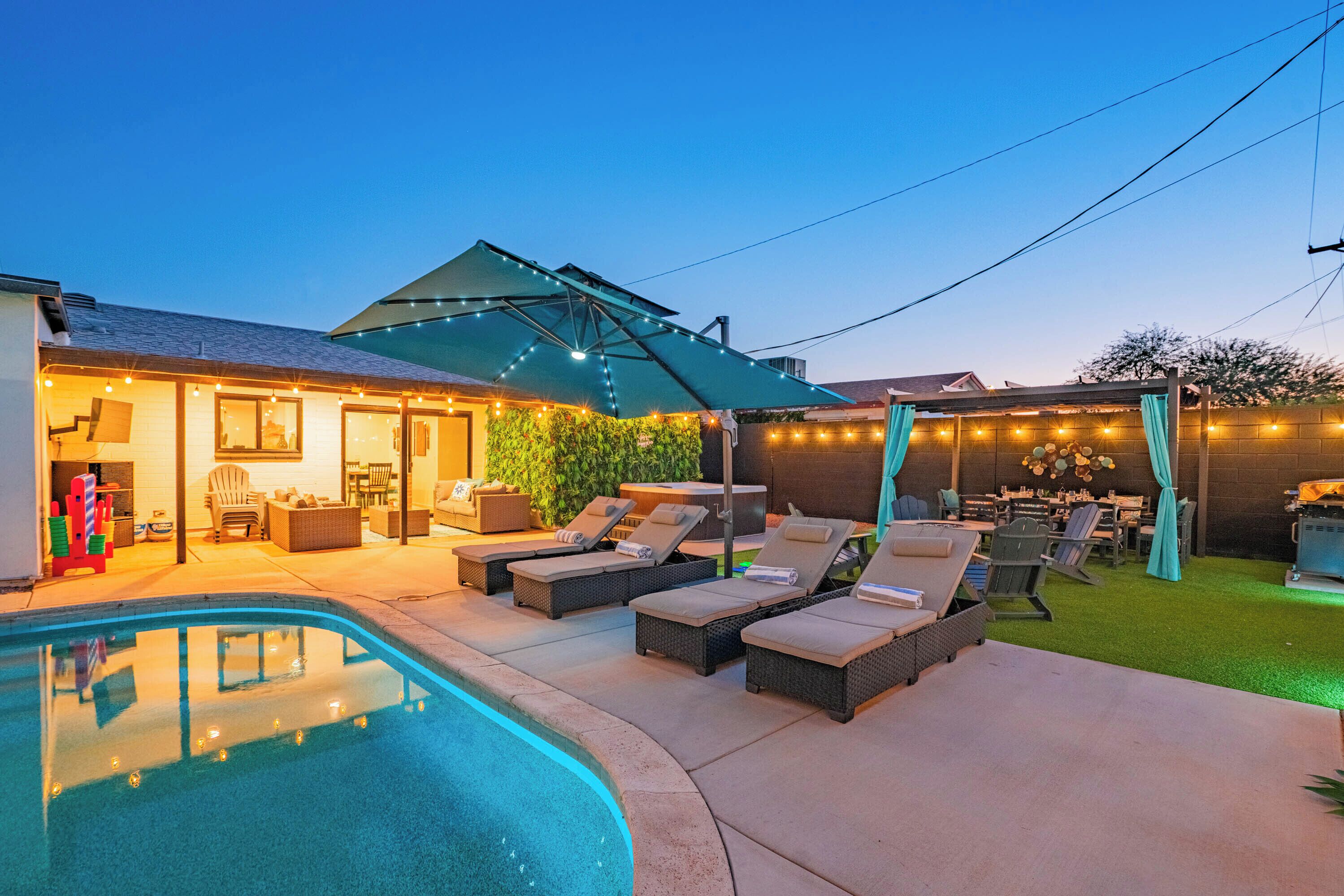A backyard with a swimming pool, lounge chairs, and a covered patio area.