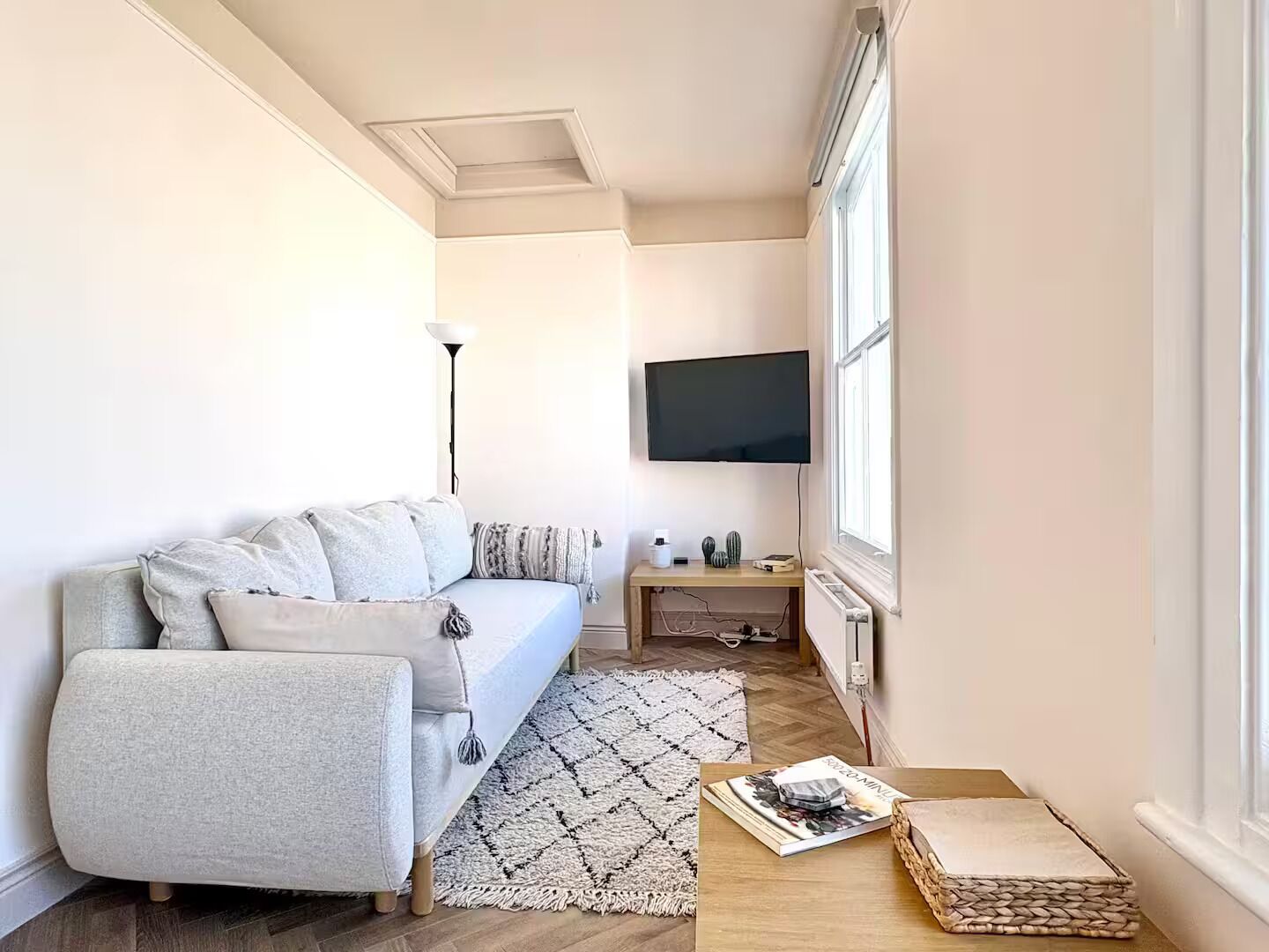 A modern living room with a sofa, a flat-screen TV, a lamp, and a small table with a magazine.
