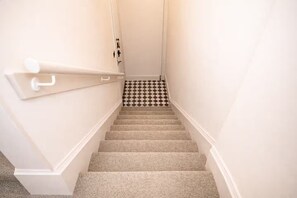 Eine Teppichstufen Treppe mit Schachbrettmuster, weißen Wänden und einer Handlauf.