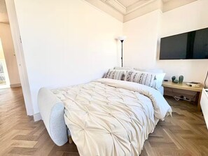 Ein Schlafzimmer mit einem großen Bett, einem Nachttisch, einer Lampe und einem an der Wand befestigten Fernseher.