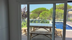 A view through a glass door of a pool area with wooden deck furniture and a clear blue sky. - Sun, sea, and Lisbon—your vacation home is waiting for you (Costa de Caparica)