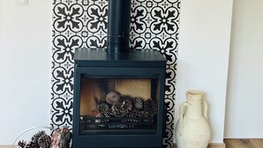 A wood-burning stove with a black chimney, a decorative wall with a geometric pattern, and a vase on the floor. - Sun, sea, and Lisbon—your vacation home is waiting for you (Costa de Caparica)