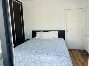 Een slaapkamer met een bed, nachtkastje, deur en een wandlamp.