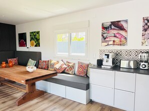 A modern kitchen with a wooden dining table, white cabinetry, and colorful artwork on the walls. - Sun, sea, and Lisbon—your vacation home is waiting for you (Costa de Caparica)
