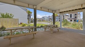 A covered outdoor area with picnic tables and a view of residential buildings in the background. - 🏄🌴Golf Cart | Steps to Beach | Multiple Balconies | Pelican Pod☀️ (Navarre)