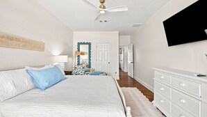 A bedroom with a bed, a dresser, a television, and a ceiling fan. - 🏄🌴Golf Cart | Steps to Beach | Multiple Balconies | Pelican Pod☀️ (Navarre)