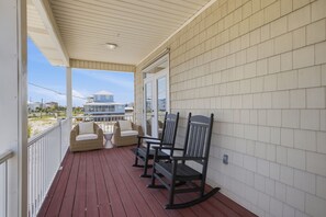 Eine überdachte Veranda mit Korbmöbeln und Blick auf Strand und Gebäude.