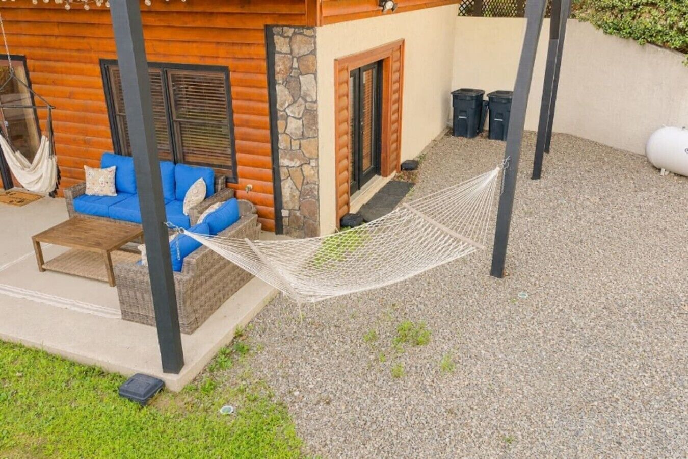A hammock between two poles, a blue sofa with cushions, and a stone wall.