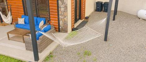 A hammock between two poles, a blue sofa with cushions, and a stone wall.
