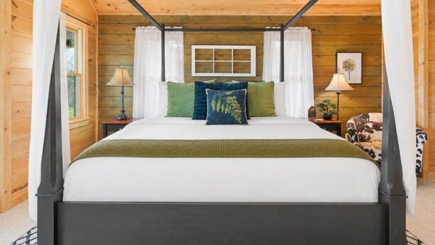 Uma cama de dossel com um edredom branco e verde, duas mesas de cabeceira com luminárias e uma poltrona com estampa de vaca.