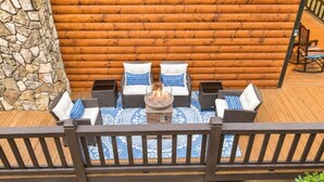 Um deck de madeira com uma parede de pedra, um poço de fogo e mobiliário de exterior.