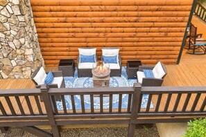 Eine Holzterrasse mit einer Steinmauer, einer Feuerstelle und Gartenmöbeln.