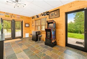 Ein Zimmer mit Holzvertäfelung, einem großen Fenster, einer Tür und einer Retro-Spielmaschine.