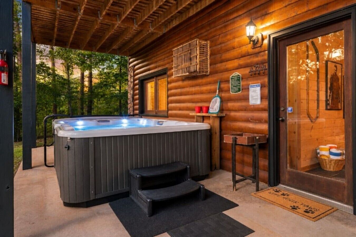 A wooden cabin with a hot tub, a wooden door, and a window with a view of trees.