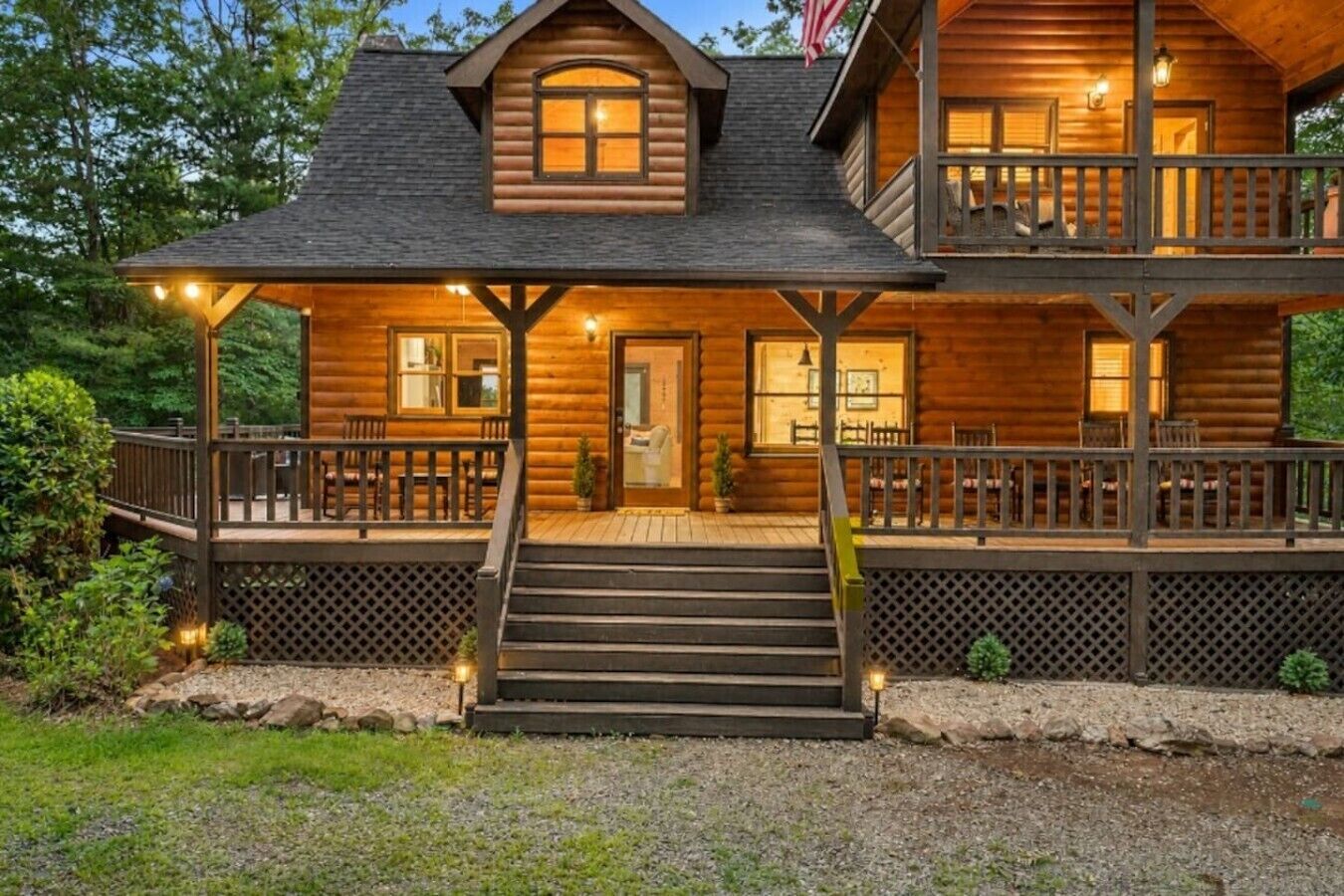 A two-story log cabin with a front porch, a staircase leading to the entrance, and a deck area.
