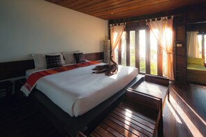 Una cama con estructura de madera, colchón blanco, almohadas y una colcha roja.