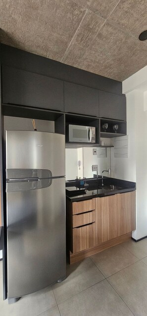 A modern kitchen with a stainless steel refrigerator, a microwave, and wooden cabinets. - On Lorena (São Paulo)
