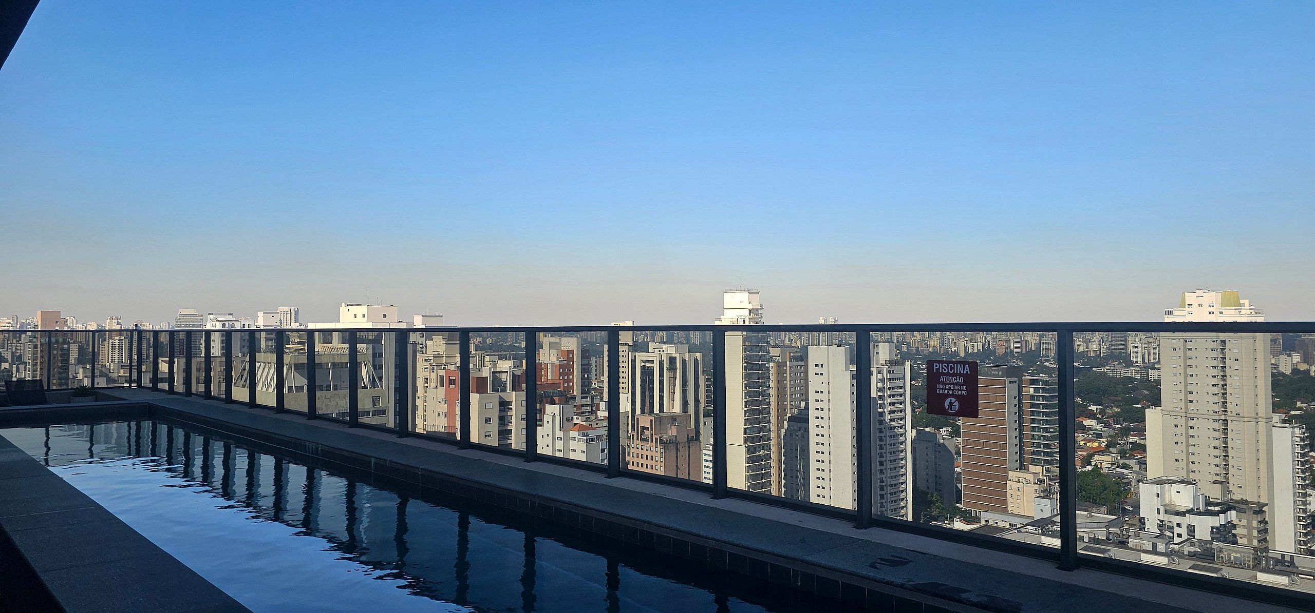 A pool with a glass barrier and a cityscape view in the background.