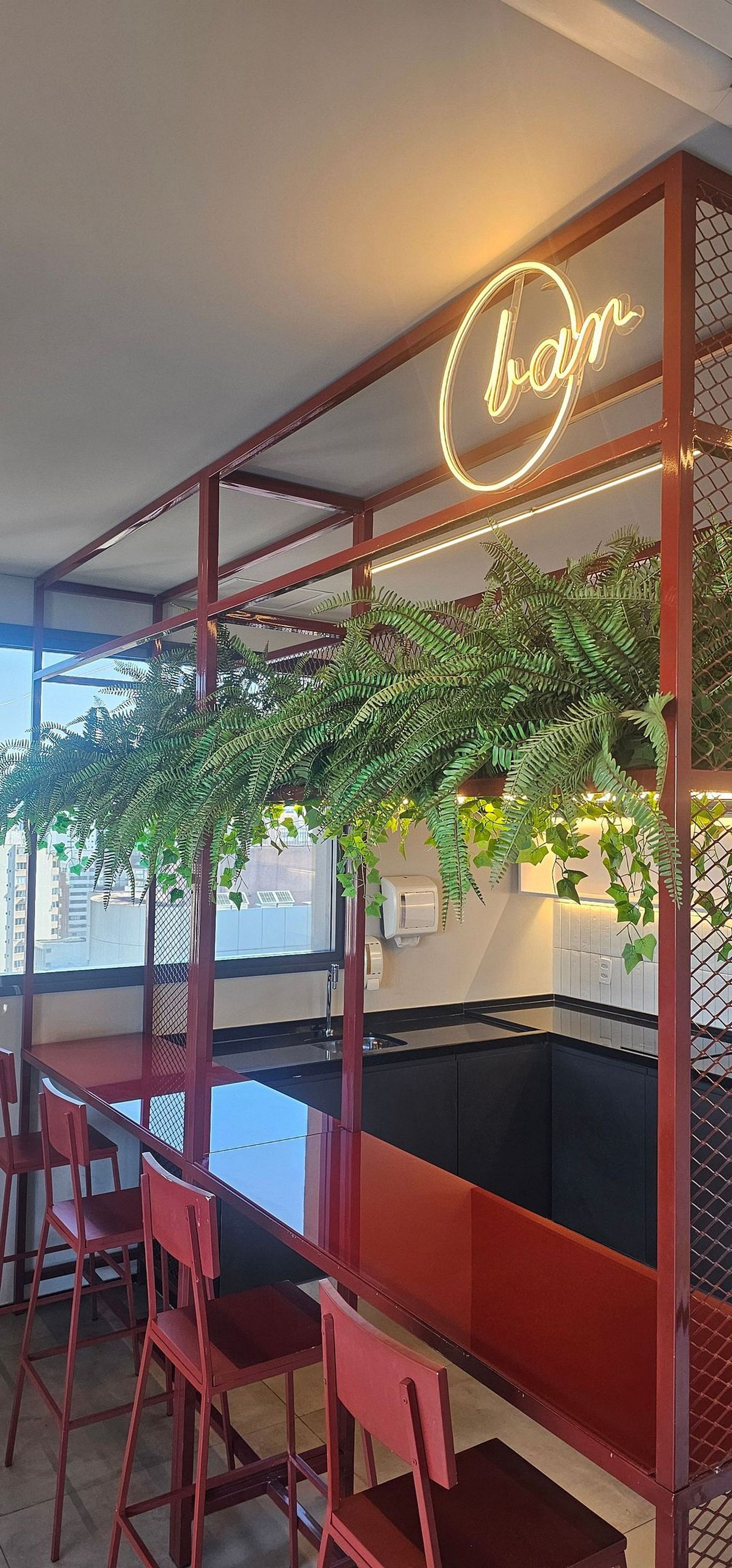 Eine moderne Bar mit einer Neonreklame, roten Stühlen und Grünpflanzen.