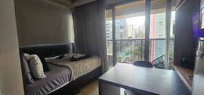A bedroom with a bed, a desk, and a window with a view of buildings. - On Lorena (São Paulo)