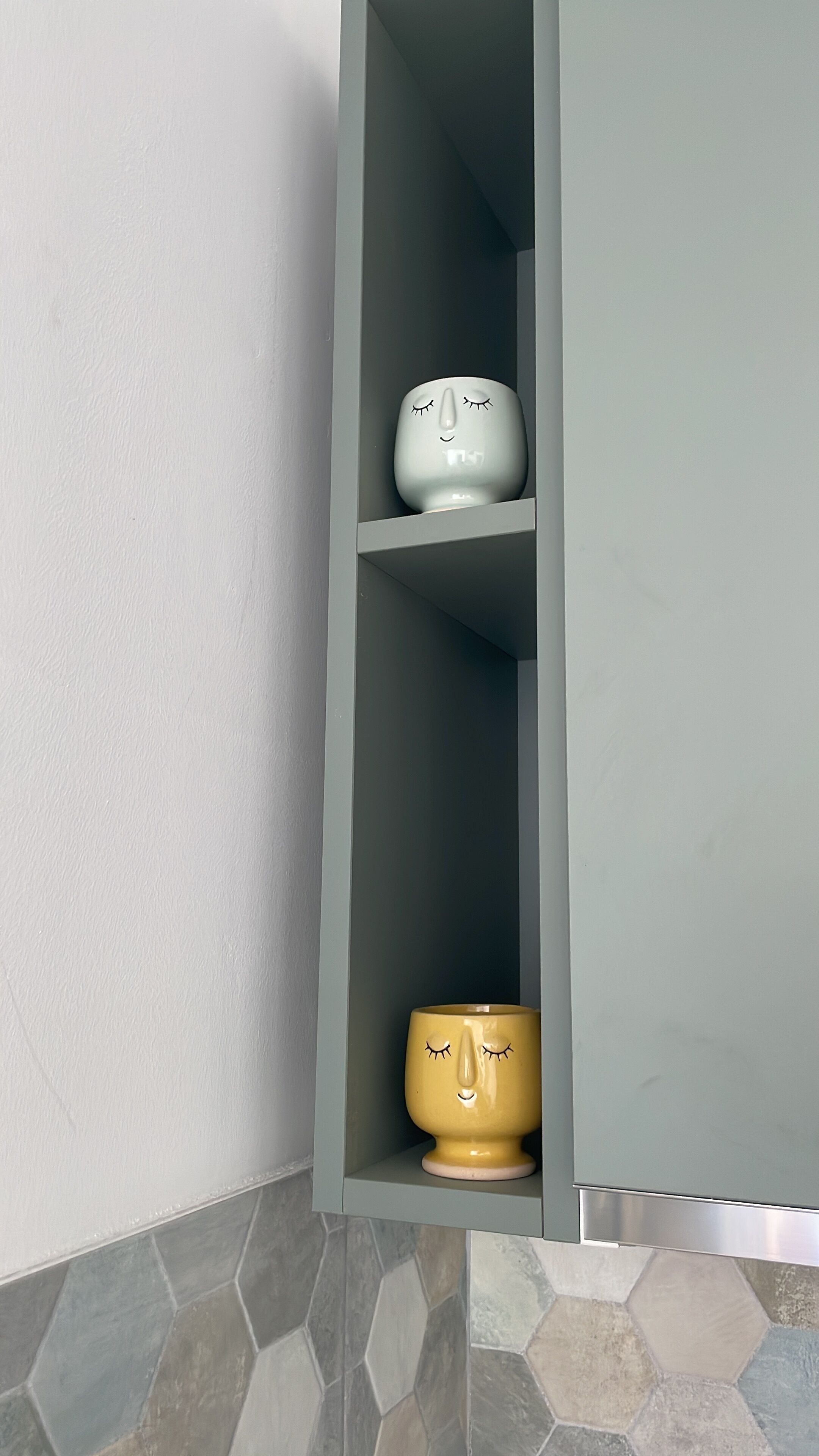 Canto de um quarto com um armário cinzento e chão de azulejos.