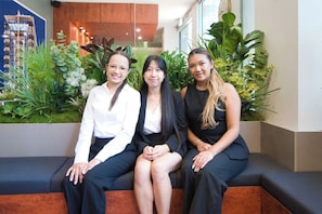 Three individuals seated on a bench in a lobby with indoor plants and a view of a building outside. - Amyra Residences on Rowlands Place - Unit 605 (Adelaide)