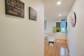 A hallway leading to a kitchen with a dining area, a clock on the wall, and artwork on the walls. - Amyra Residences on Rowlands Place - Unit 605 (Adelaide)