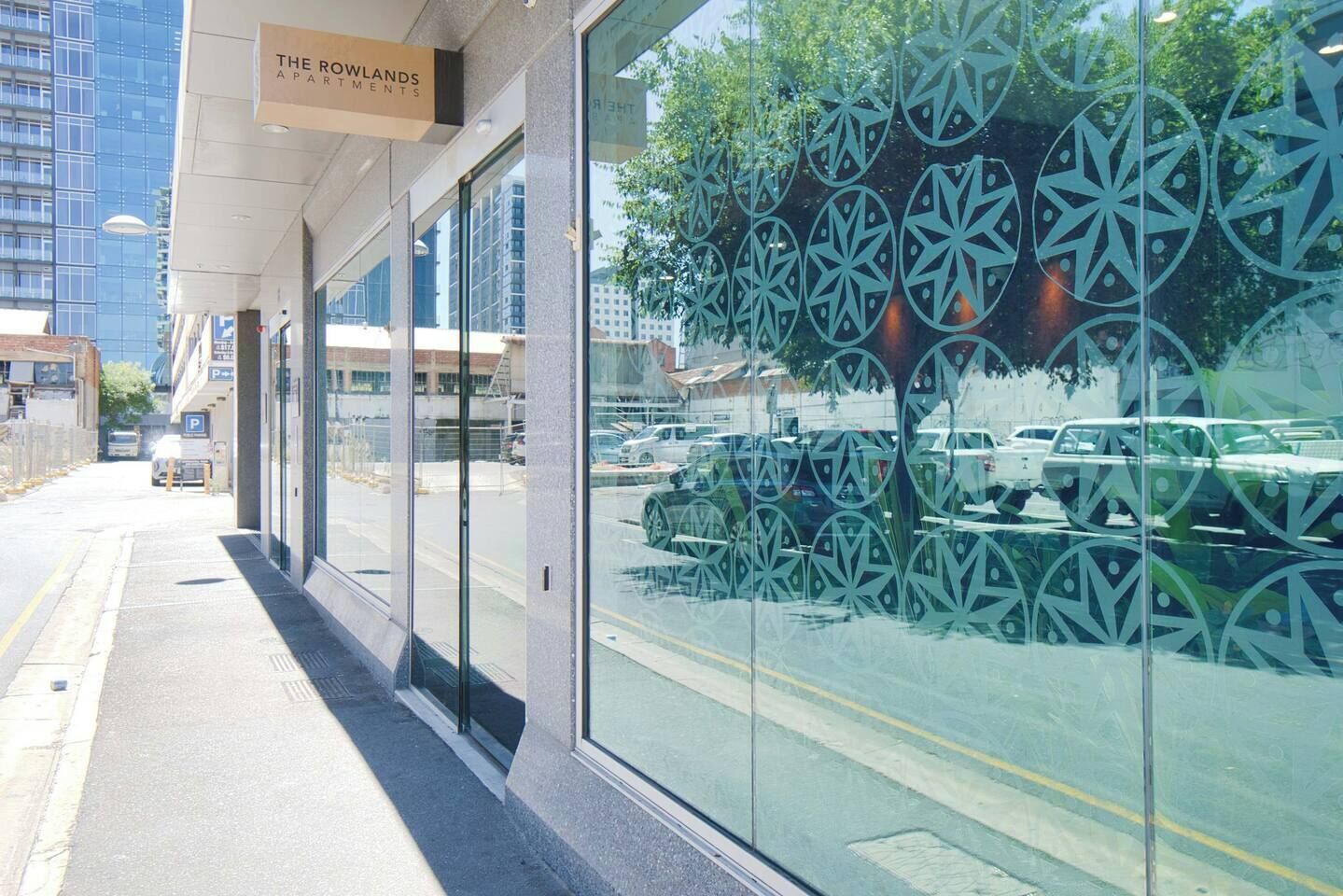 A modern building with a glass facade and a sign reading 'The Rowlands Apartments.'