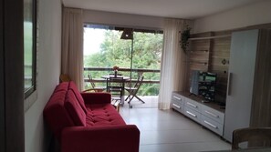 A living room with a red sofa, a dining table with chairs, a TV, and a sliding glass door leading to a balcony. - An excellent bungalow for relaxing, located on Pescaria Beach in Maceió (Maceió)