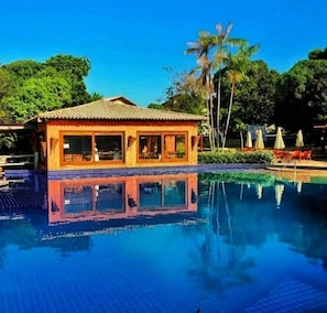 A poolside building with a tiled roof and windows, surrounded by a clear blue pool reflecting the sky. - An excellent bungalow for relaxing, located on Pescaria Beach in Maceió (Maceió)
