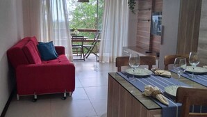 Uma sala de estar moderna com um sofá vermelho, uma mesa de jantar posta para dois e vista para o exterior.