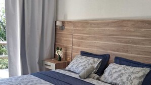 A modern bedroom with a wooden headboard, a large bed with floral bedding, a nightstand with a vase, and a window with curtains.