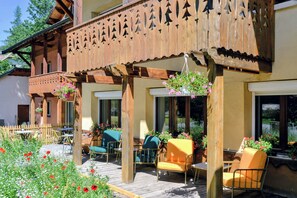 A wooden balcony with a decorative railing, outdoor seating with chairs and tables, and hanging flower baskets. - ABRIES HOTEL  (Abriès-Ristolas)